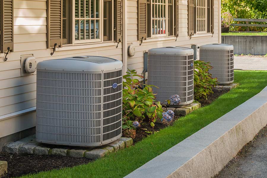 Three outdoor air conditioning units beside a house