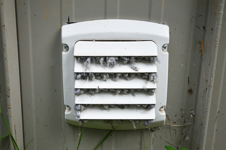 A white vent cover on a gray wall clogged with lint.